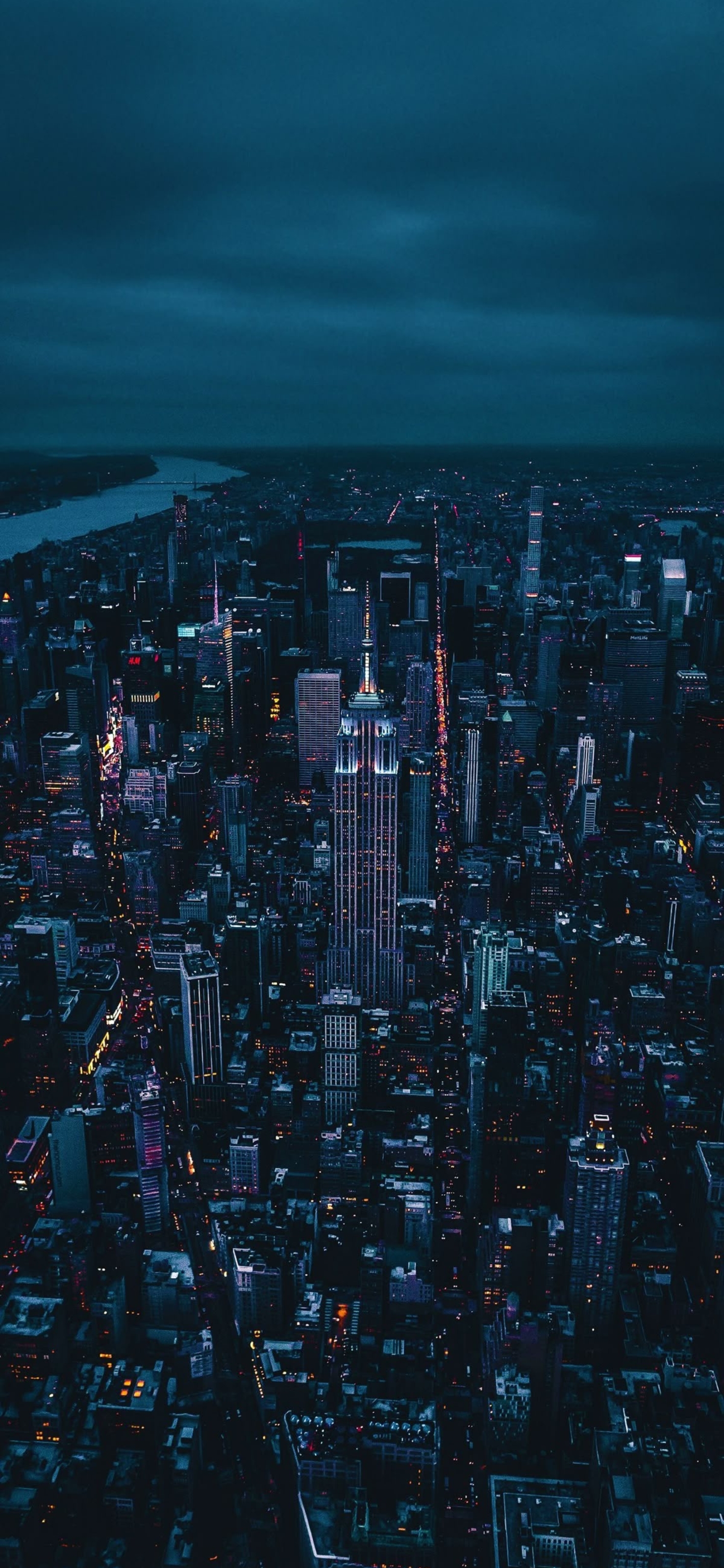 Nighttime cityscape with illuminated skyscrapers, vibrant lights, and moody sky | Blue, Black, Purple | 4K Wallpaper for Mobile