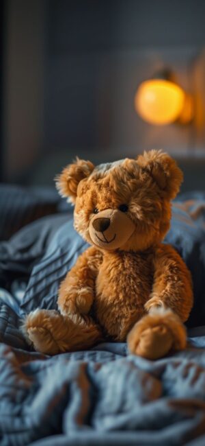 Cuddly teddy bear on a quilted bed with warm amber light ambiance in a cozy room | 4K Wallpaper, for Mobile