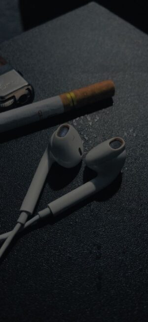 Pair of white earphones, a cigarette, and lighter on a textured black surface | Moody contrast | 4K Wallpaper for Mobile