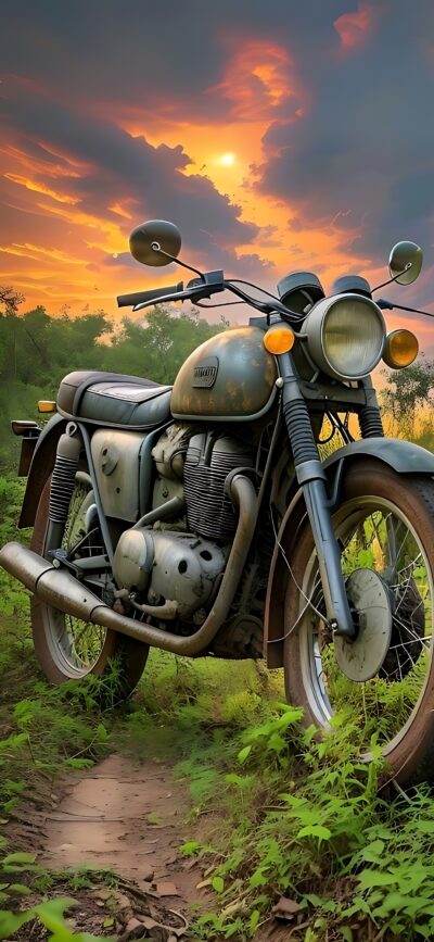 Vintage motorcycle on grassy path at sunset with vibrant clouds | Green, Orange, Yellow | 4K Wallpaper for Mobile