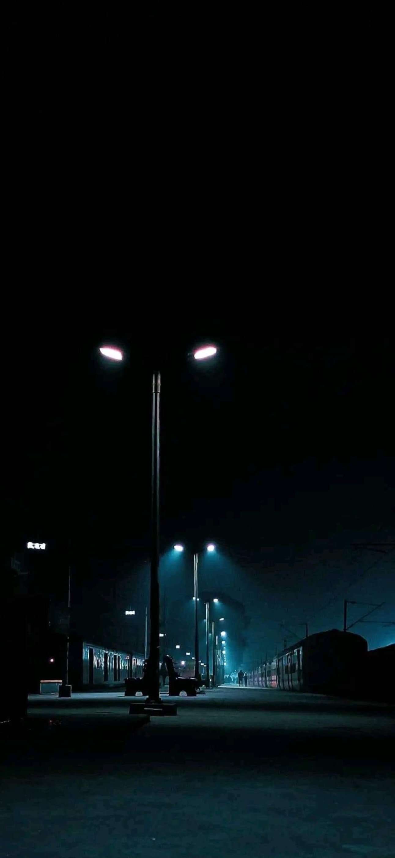 Dimly lit night train station platform, moody urban vibe, streetlights illuminate, black & blue tones. | 4K Wallpaper for Mobile