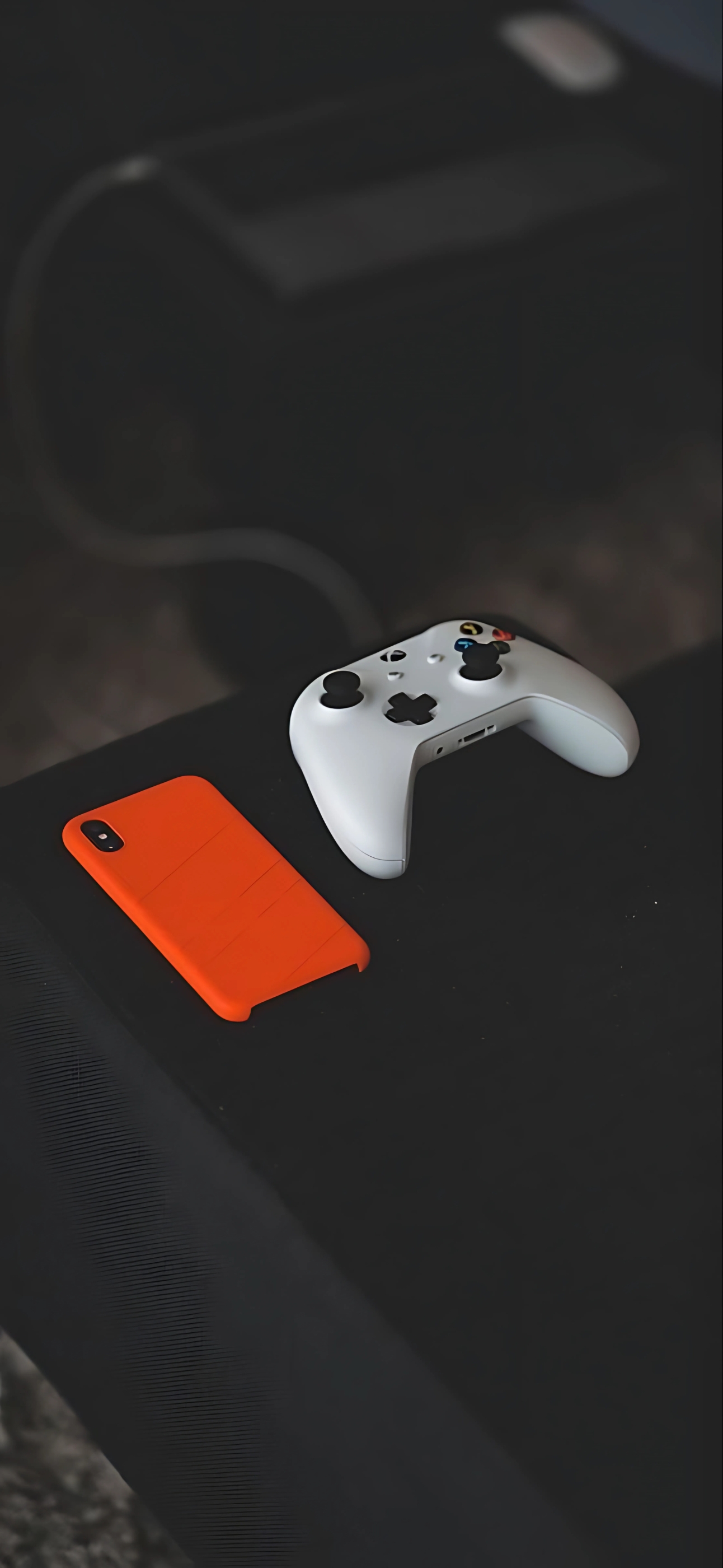 Gaming controller & orange phone case on dark background | Tech & gaming focus | Black, white, & orange tones | 4K Wallpaper for Mobile