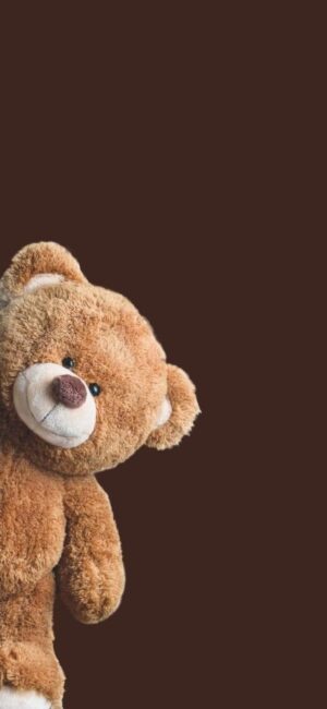 Teddy bear peeks from left on a dark brown background, showcasing cute and fluffy features. | 4K Wallpaper, for Mobile | Brown Wallpaper