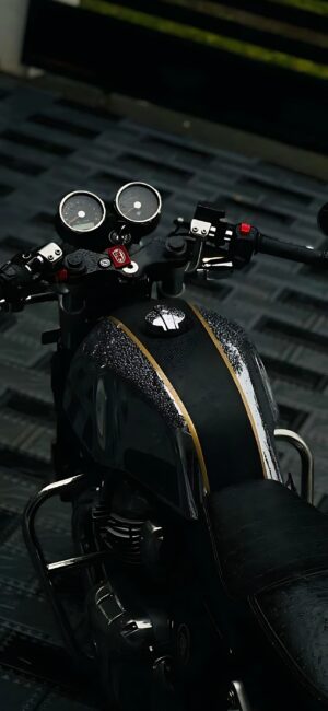 Close-up of a motorcycle dashboard with analog dials, sleek handlebars, and a wet fuel tank in black and gold | 4K Wallpaper for Mobile