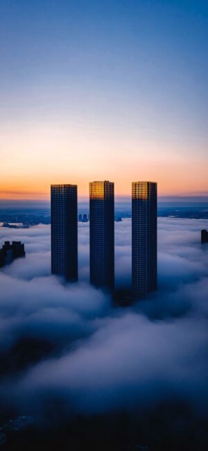 Cityscape at sunrise with skyscrapers in clouds, highlighted by golden sunlight. Deep blue sky creates a stunning contrast | 4K Wallpaper for Mobile