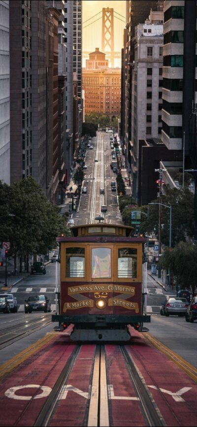 San Francisco cable car on steep street with Golden Gate Bridge at sunset, highlighting urban charm. | 4K Wallpaper for Mobile