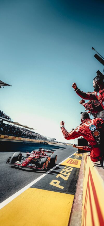 Formula 1 race scene with a red car and celebrating crew under a clear blue sky, emphasizing speed and victory | 4K Wallpaper, for Mobile