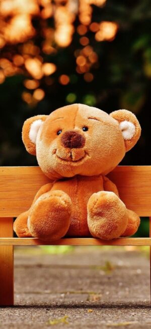 Cute teddy bear on a wooden bench with blurred background focusing on its expression and texture | 4K Wallpaper for Mobile