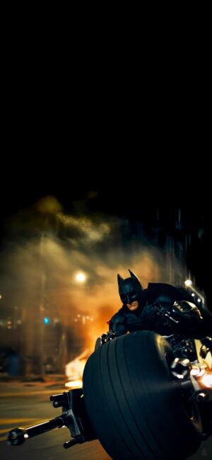 Batman on Batcycle in a dramatic city nightscape, embodying justice with black, orange, yellow hues | 4K Wallpaper for Mobile.