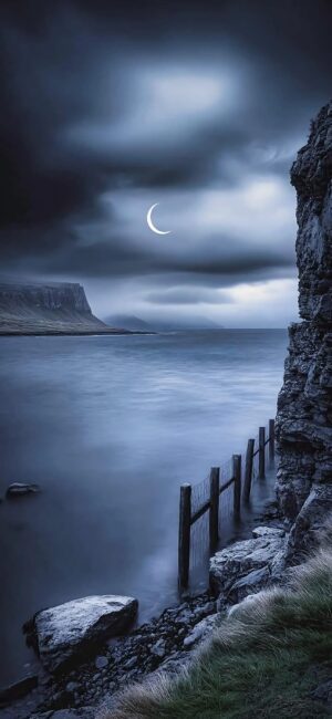 Serene seascape at night with crescent moon, cloudy sky, and rustic fence | Blue, Black, Gray | 4K Wallpaper for Mobile