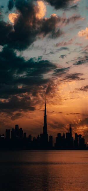 Cityscape skyline silhouetted at sunset with dramatic clouds, orange and yellow hues | 4K Wallpaper for Mobile