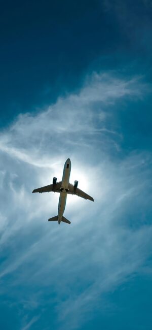 Airplane soaring against a blue sky with wispy clouds and sunlight halo effect | 4K Wallpaper | for Mobile