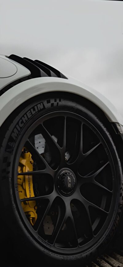 Close-up of a black alloy car wheel with a Michelin tire and yellow Porsche brake caliper, highlighting vehicle sophistication | 4K Wallpaper for Mobile