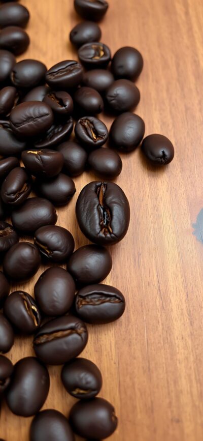 Close-up dark roasted coffee beans on a wooden surface, rich textures & earthy hues | 4K Wallpaper for Mobile