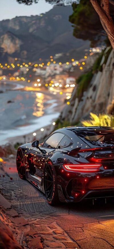 Sleek black sports car on coastal road at sunset, ocean view, city lights, mountains, and greenery | 4K Wallpaper for Mobile.