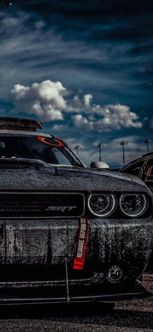 Dodge Challenger SRT under dramatic clouds, showcasing powerful front view and moody atmosphere | Black, Gray, Blue | UHD Wallpaper for Mobile