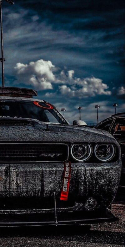Dodge Challenger SRT under dramatic clouds, showcasing powerful front view and moody atmosphere | Black, Gray, Blue | UHD Wallpaper for Mobile